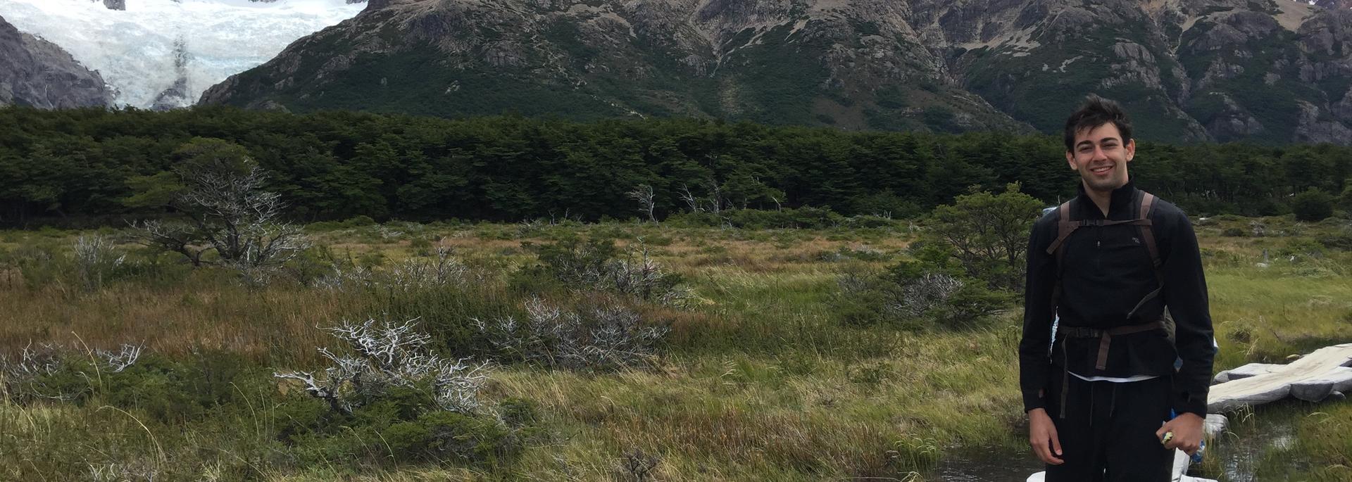 Hiker standing on a trail with snowy mountains behind.